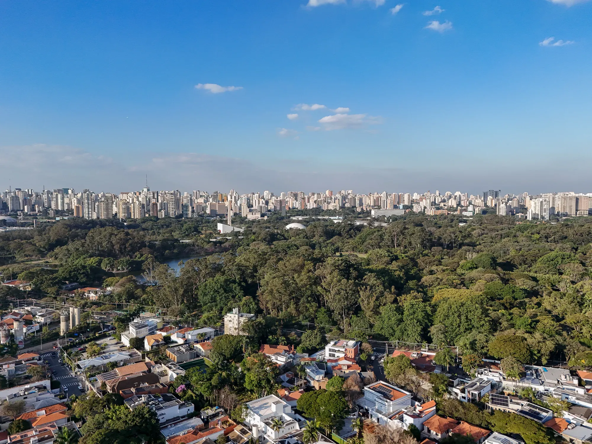 Wide aerial view of Ibirapuera Park and the surrounding São Paulo skyline under a clear blue sky