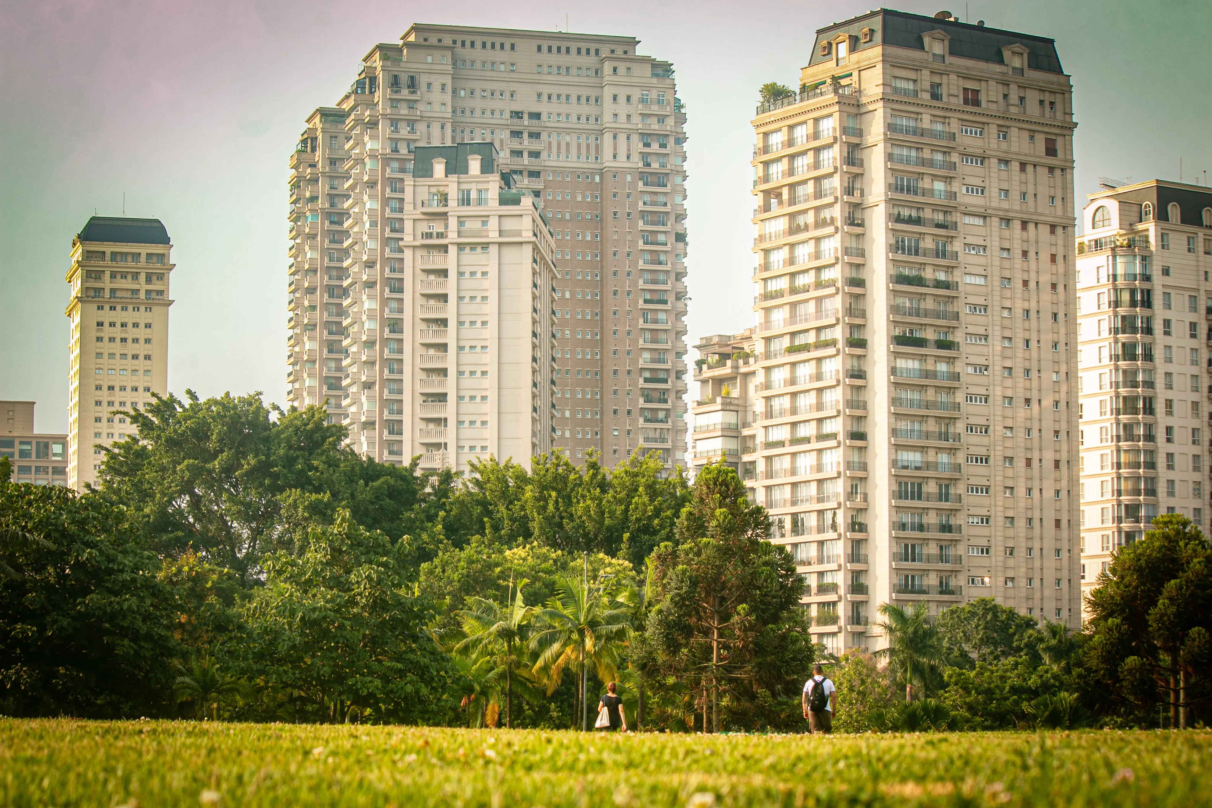 High-rise residential towers behind trees and a grassy field with two pedestrians