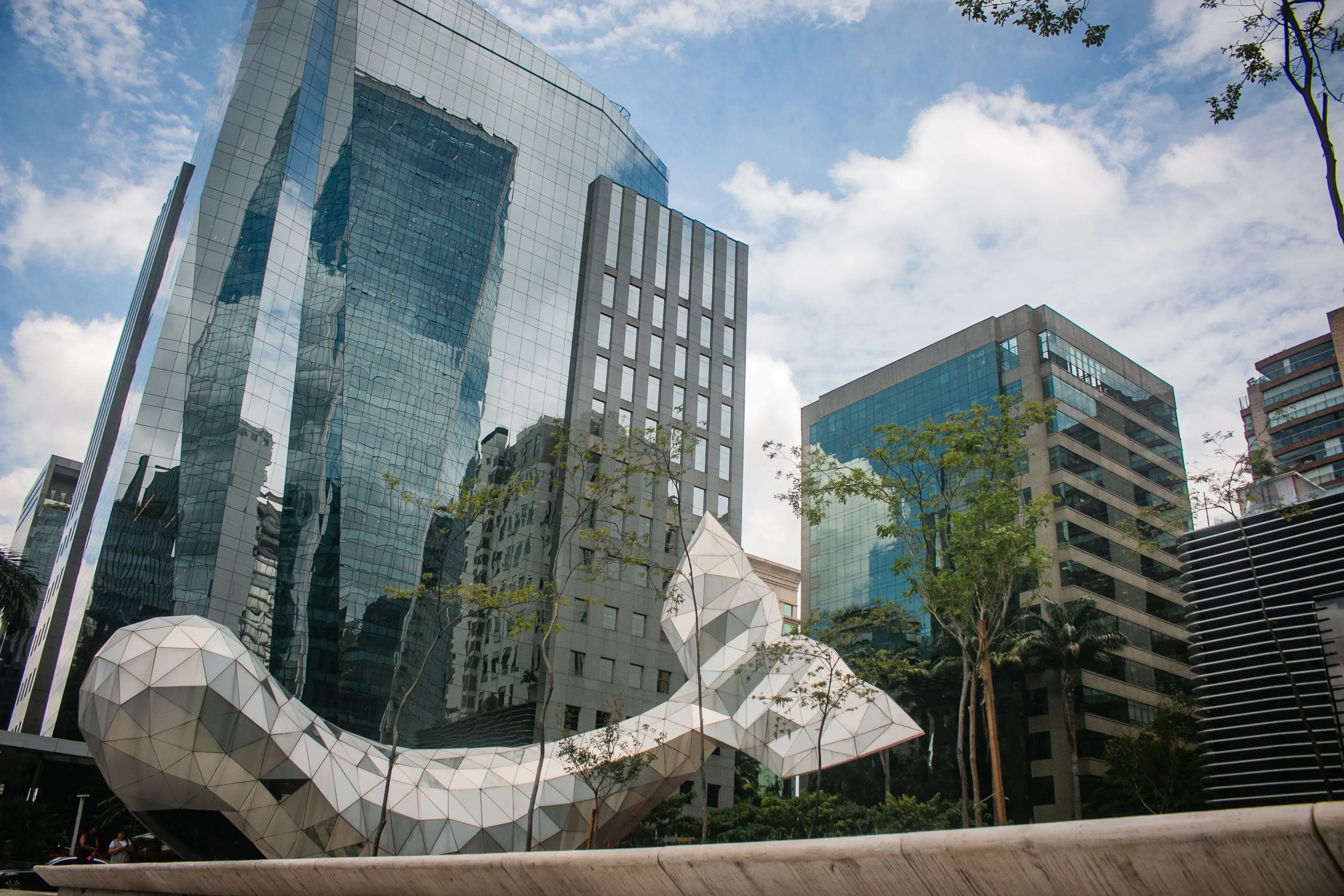 Modern glass office towers with a geometric white sculpture in an urban plaza