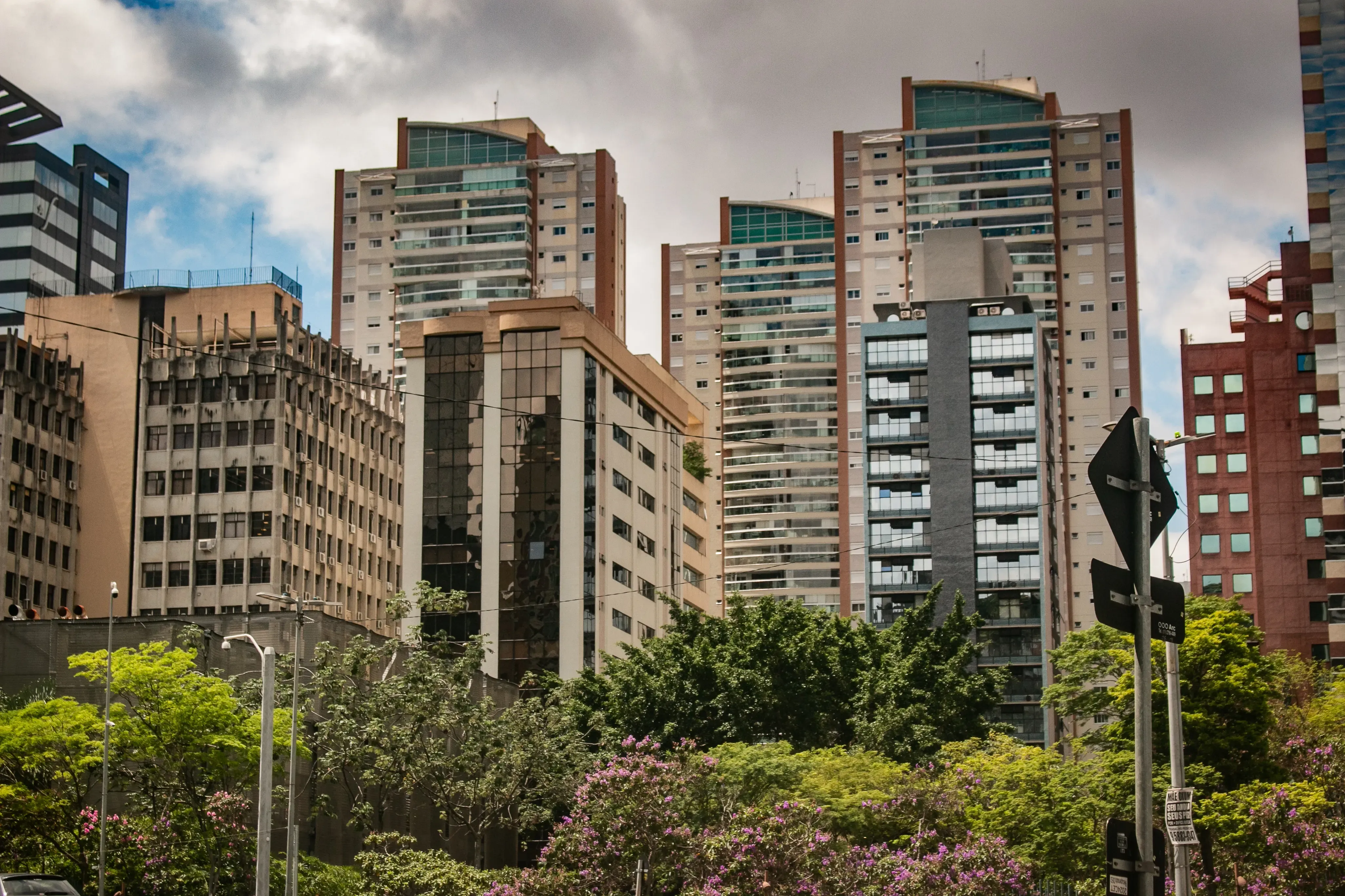 Cluster of mid- and high-rise buildings behind trees under a cloudy sky