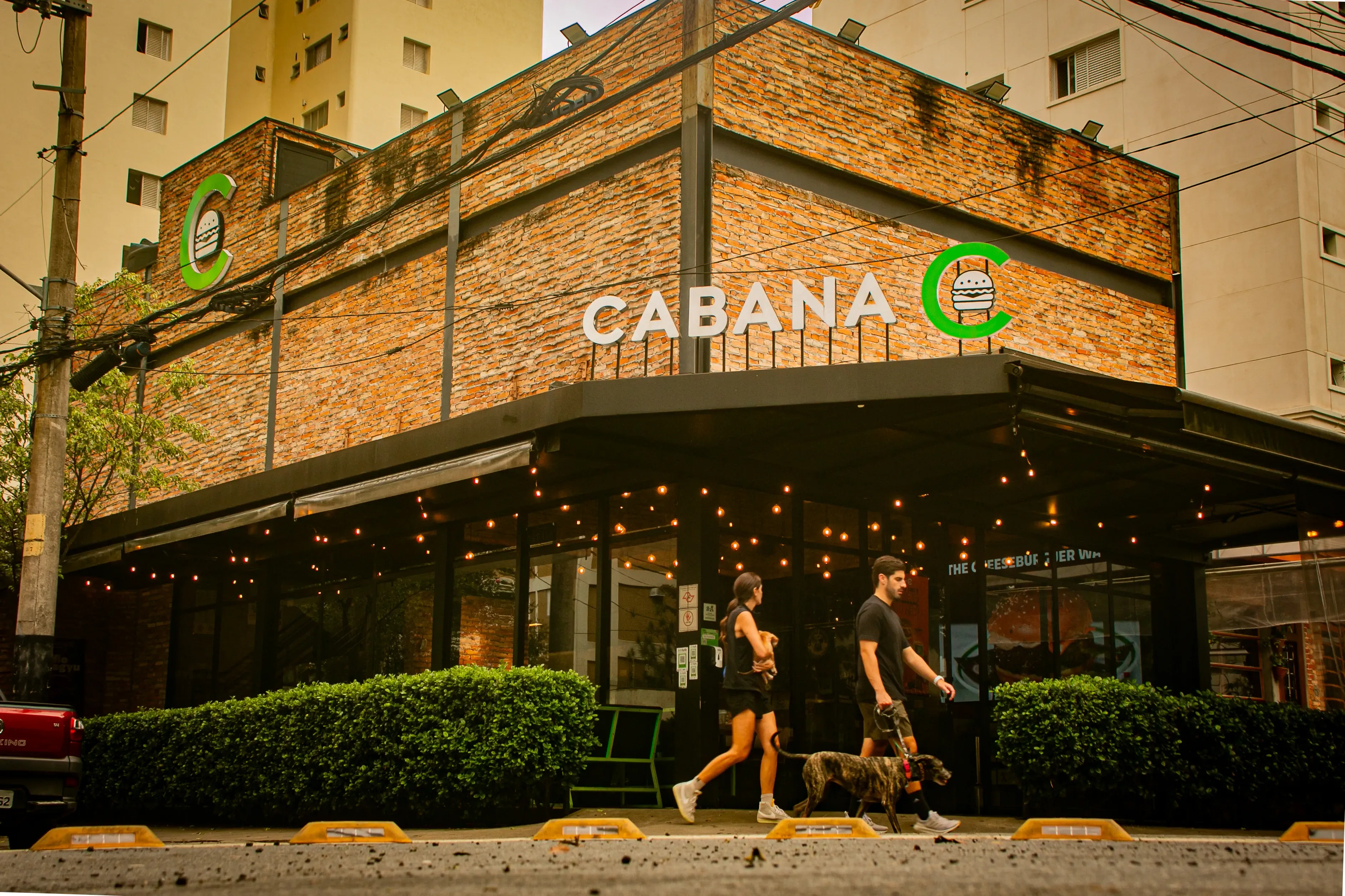 Facade of Cabana restaurant in Moema, with pedestrians and a dog on the sidewalk